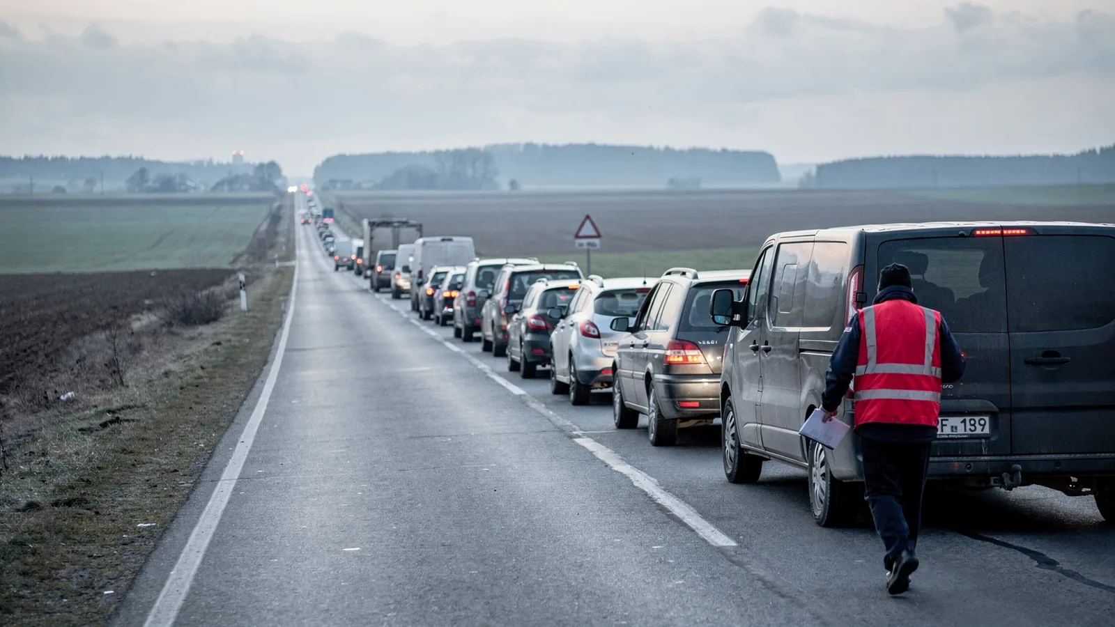 Vodič s podložkou obchádza dodávku zaparkovanú v rade vozidiel pred hraničným priechodom
